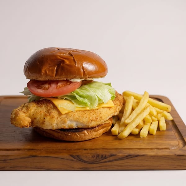 Crispy chicken sandwich with cheese, lettuce, tomato, and fries on a wooden board.