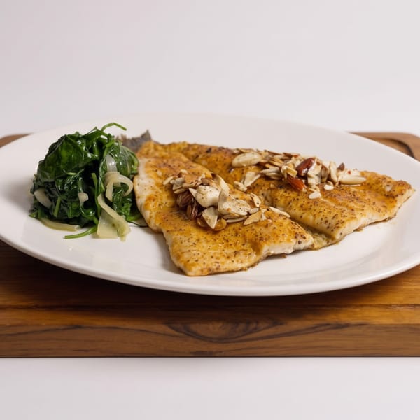 Two almond-crusted fish fillets with a side of sautéed spinach and onions on a white plate.