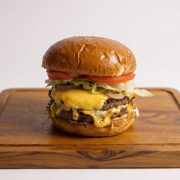 Double cheeseburger with melted cheese, lettuce, tomato, and onions on a wooden board.